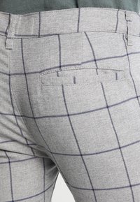Szare spodnie w kratę z granatowymi liniami, z pasem i tylną kieszenią, wykonane z teksturowanej tkaniny.