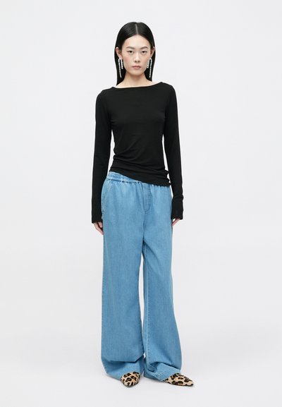 Camisola preta de mangas longas combinada com calças azuis de ganga largas. Footwear com padrão de leopardo. Design simples e texturas suaves.