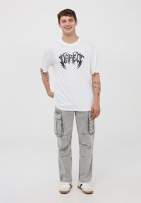 Biała bawełniana koszulka z czarnym nadrukiem na piersi, w połączeniu z jasnoszarymi spodniami cargo z wieloma kieszeniami i luźnym krojem.