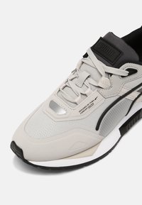 Baskets Puma grises et noires avec lacets blancs, dessus en mesh, et texte « Designed by Puma Forever Faster » près de la zone des orteils.