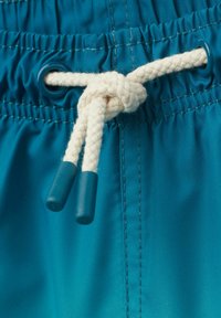 Bañadores de color aqua con una cinturilla elástica, que cuentan con un cordón blanco trenzado con puntas de plástico aqua y detalles cosidos.