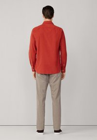 Rotes Langarmhemd mit Button-Down-Kragen, kombiniert mit hellbraunen karierten Hosen und braunen Schuhen, von hinten betrachtet.
