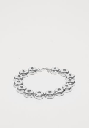 Silberarmband mit runden, polierten Metallringen und einem zentralen Ausschnitt, mit einem Verschluss gesichert, auf einem weißen Hintergrund präsentiert.