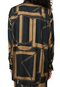 Sort og guld mønstret skjorte med geometriske designs, lange ærmer og en afslappet pasform. Glat, skinnende stof med knapdetaljer ved manchetterne.