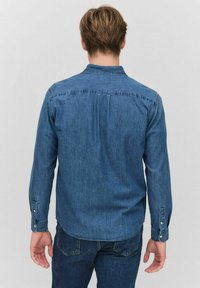 Pitkähihaiset farkkupaita keskisinisessä, jossa on nappikaulus, nappikiinnitys hihoissa ja kaareva helma takana oleva sauma. 