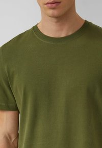 Olijfgroene katoenen T-shirt met een ronde hals, korte mouwen en een gladde textuur. Heeft zichtbare stikseldetails bij de hals.