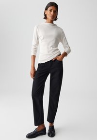 Weißes Langarmoberteil mit rundem Halsausschnitt, kombiniert mit schwarzen geraden Hosen und schwarzen Slippern. Glattes Material mit minimalen Details.