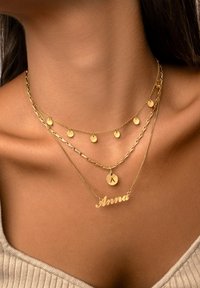 Gold-vergoldete Halskette mit drei Strängen: einer mit runden Anhängern, einer mit Kettengliedern und einer mit einem personalisierten Namensschild.