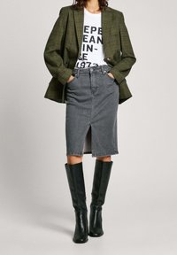 Groene geruite blazer, wit T-shirt met print, grijze denim kokerrok met voorsplit en zwarte leren laarzen met hak tot over de knie.