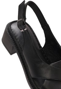 Sandale en cuir noir avec un bout fermé et un talon ouvert, dotée d'un talon carré épais, d'une bride de cheville ajustable et d'un motif texturé sur la semelle.