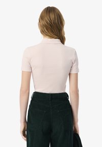 Vaaleanpunainen ribbipaita, jossa on käänteellinen kaulus, ja tummanvihreät corduroypantsit korkealla vyötäröllä, joissa on takataskut.