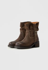 Bruna läderankelboots med en viksfald, dekorativ söm och en sidspänne. Klossheel med texturerad yta.