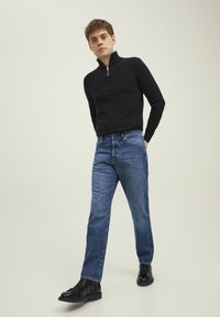 Svart zip-neck genser, blå jeans og glansete svarte støvler. Jeansene er rettsnittede med en lett falming og fem-lommers design.