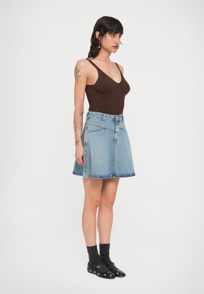 Καφέ πλεκτό κορμάκι με λαιμόκοψη V, σε συνδυασμό με μπλε τζιν φούστα A-line. Σημαντικές λεπτομέρειες περιλαμβάνουν υφή υφάσματος και ξεφτισμένο τελείωμα.