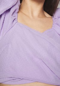 Lavendelfärgad cropped top i texturerad tyg. Den har puffärmar och en fyrkantig halsringning med ett lagerdesign.