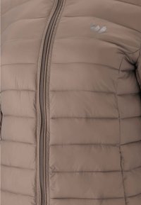 Veste matelassée taupe avec couture horizontale, fermeture éclair avant, poche latérale et petit logo réfléchissant sur la poitrine.