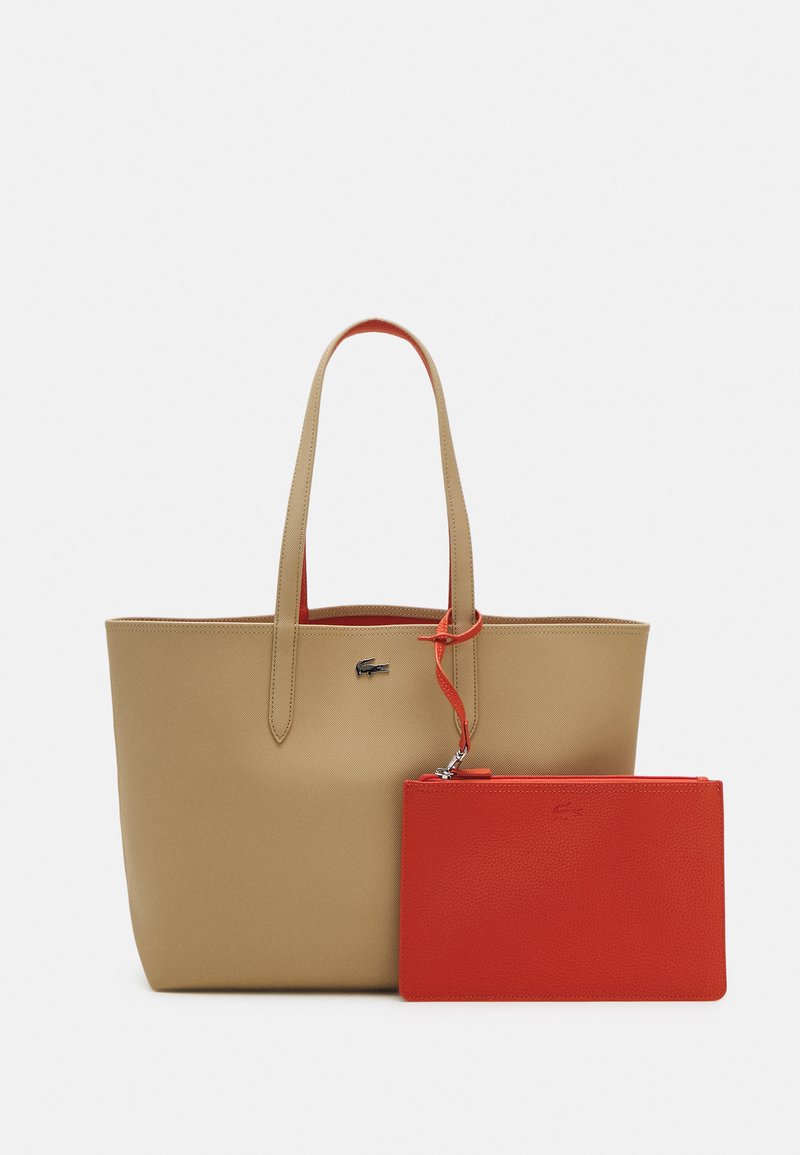 Bolso tote beige con textura suave y dos asas largas, que incluye un pequeño estuche rojo con textura de guijarros, ambos con detalles de logo.