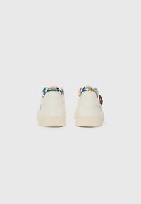 Baskets blanches avec une texture lisse, arborant un motif floral coloré au dos du col et une semelle en caoutchouc couleur crème.