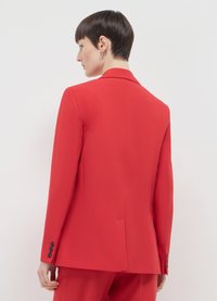 Blazer rosso su misura in tessuto liscio, con rever a lancia, spacco singolo posteriore e polsini a quattro bottoni con bottoni neri.
