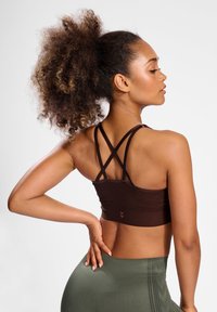 Bruine sportbh met gekruiste banden, textuurstof en logodetail, gecombineerd met hoge, olijfgroene legging met een patroon.