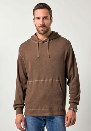 Bruine hoodie gemaakt van gestructureerde stof, met een voorvak en geribbelde manchetten. Gecombineerd met blauwe jeans.