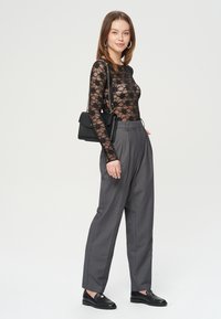 Czarny koronkowy bodysuit z długim rękawem w kwiatowy wzór, w zestawieniu z szarymi spodniami o wysokim stanie i czarnymi loafersami. Czarna torebka jako dodatek.