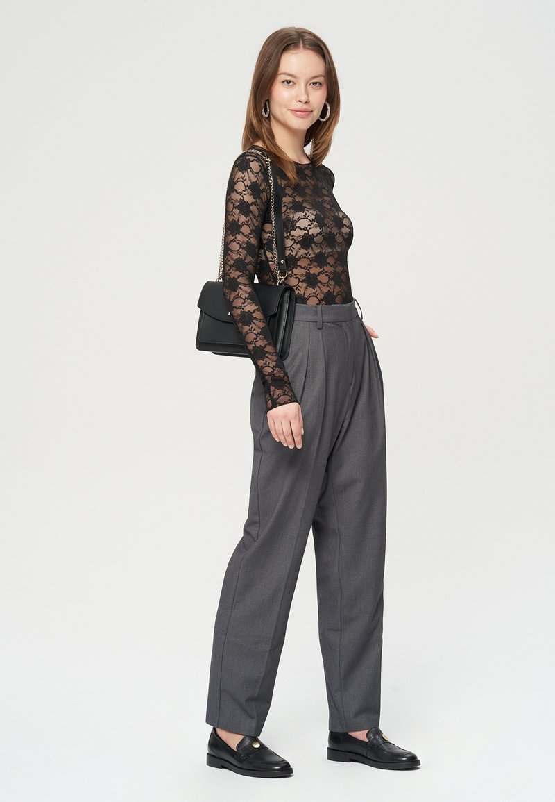 Czarny koronkowy bodysuit z długim rękawem w kwiatowy wzór, w zestawieniu z szarymi spodniami o wysokim stanie i czarnymi loafersami. Czarna torebka jako dodatek.