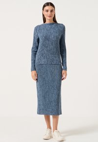 Completo blu lavorato a maglia composto da un top a maniche lunghe e una gonna di lunghezza media con un motivo testurizzato a coste. Vestibilità casual, abbinato a sneakers bianche.
