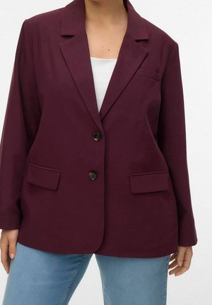 Frau trägt einen dunkelvioletten Blazer mit zwei Fronttaschen und Knöpfen, kombiniert mit hellblauen Jeans und einem weißen Top darunter.