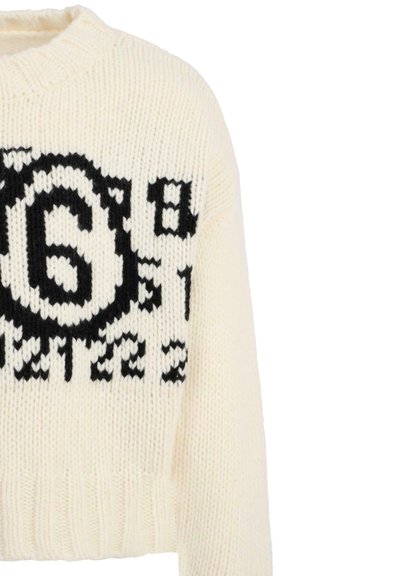 Kremowy sweter z dzianiny z czarnym grafiką i tekstem. Posiada okrągły dekolt i ściągacz u dołu. Krótka długość.