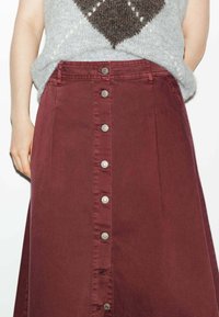 Jupe A-line bordeaux avec fermeture à boutons sur le devant, dotée de quincaillerie en ton argent et d'une texture en coton lisse.