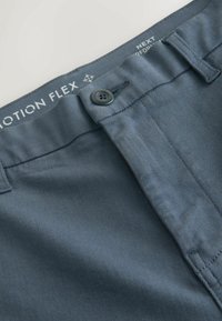 Sötétkék nadrág rugalmas anyagból, gombos záródással, sík elejű kialakítással és finom mintázattal, a márkajelzés a derékrészen található.