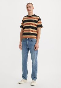 Zwart en gele gestreepte t-shirt met korte mouwen, gecombineerd met lichtblauwe jeans en crèmekleurige sneakers. Casual pasvorm, minimale branding.