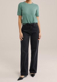 Lichtgroen geïndukt brei top met korte mouwen, gecombineerd met hoge zwarte rechte jeans en puntige zwarte ballerina's.