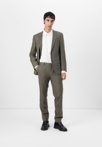 Olive green tailored suit with a slim fit, paired with a white button-up shirt. Details include a single-breasted jacket and black shoes.