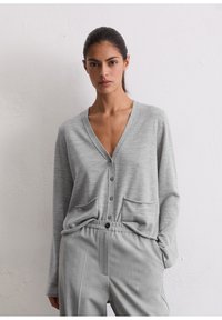 Cardigan grigio con scollo a V, chiusura a bottoni e due tasche frontali. Abbinato a pantaloni grigi coordinati, entrambi in un tessuto morbido e testurizzato.
