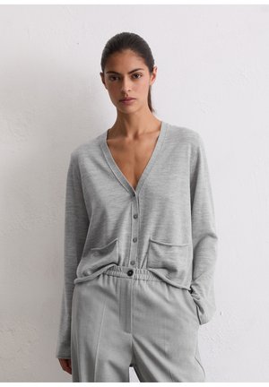 Cardigan gris avec un col en V, fermeture à boutons et deux poches frontales. Associé à un pantalon gris assorti, les deux en tissu doux et texturé.