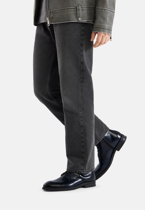 Granatowe skórzane eleganckie buty z zaokrąglonym noskiem, zestawione z ciemnoszarymi jeansami, prezentujące gładką fakturę i subtelne detale przeszyć.