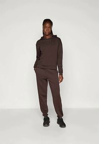 Brun bomullshuvtröja med dragsko och matchande joggapants. Mjuk textur, avslappnad passform och svarta sneakers fulländar outfiten.