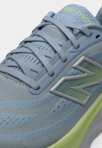 Κοντινό πλάνο ανοιχτό μπλε αθλητικού παπουτσιού με πράσινη σόλα, λεπτομερείς κορδόνια και λογότυπο New Balance στο πλάι.