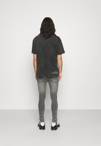 Camiseta de gran tamaño en color negro con efecto mineral y mangas cortas, combinada con jeans skinny grises con tobillos con cremallera y zapatillas negras.