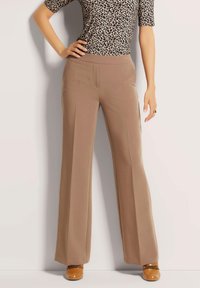 Beige wijde broek met een gladde textuur, met voorplooien, gedragen met een zwart en tan luipaardprint top en tan schoenen.