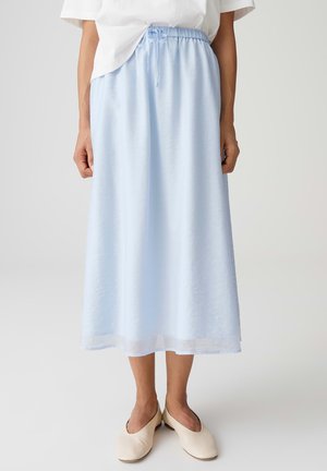 Hellblauer Midirock mit elastischem Bund und Kordelzug, kombiniert mit cremeweißen flachen Schuhen und einem in den Rock gesteckten weißen Oberteil.