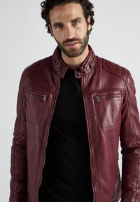 Burgunderfarbenes Lederjacke mit Stehkragen, Reißverschlusstaschen und gesteppter Schulterdetails. Glatte Textur und figurnahe Passform.