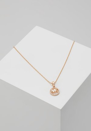 Collier en or rose avec un pendentif circulaire portant les initiales "MK" entouré d'une bordure de strass. La chaîne présente une finition texturée.