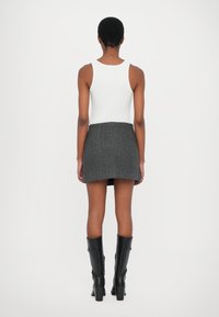 Svart tweed mini-skjørt med rett snitt, kombinert med en hvit tank-top og svarte høyhælte støvler til kneet. Jevn tekstur, ingen synlige mønstre.