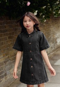 Robe en denim noir avec manches courtes, boutonnage à l'avant et col classique. Le tissu présente une finition texturée avec des coutures visibles.