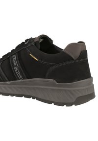 Scarpa sportiva nera con esterno in pelle scamosciata, suola in gomma grigia e dettagli in cucitura. Presenta un collo imbottito e una linguetta imbottita.