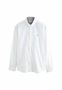 Chemise blanche à manches longues en coton, dotée d'un col et d'un petit emblème brodé. Intérieur doublé d'un motif à carreaux.