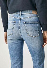 Jasnoniebieskie dżinsy o slim fit, posiadające dwie tylne kieszenie i przeszycia. Pasek w talii ozdobiony jest skórzaną naszywką z logo.